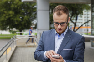 Caucasian businessman outside office using mobile phone on a office block background. Copy space